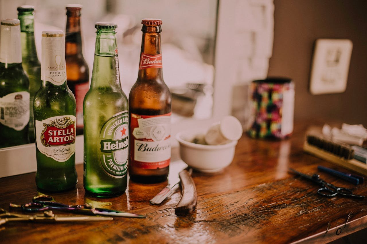 Beer bottles and barber tools on a wooden barbershop counter with a blurred mirror reflection.